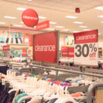 Red clearance sign for 30 off on cloth rack with variety of women apparel in retail store.