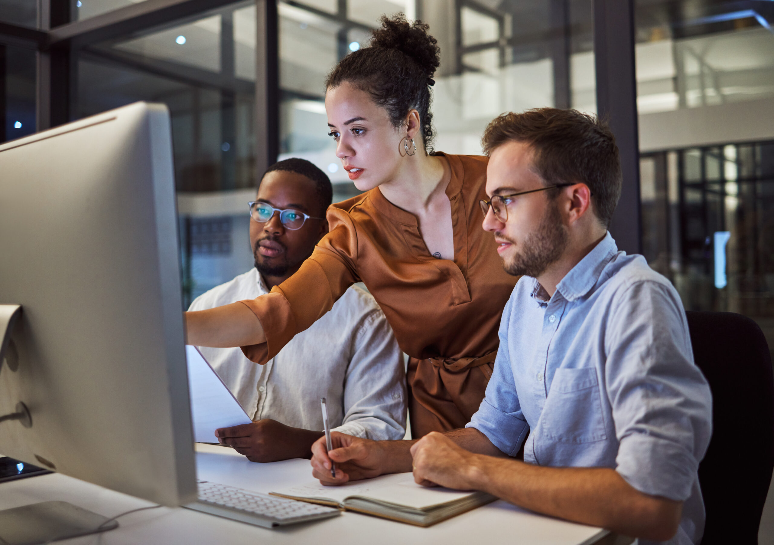 Team of coworkers sitting around a computer at a desk.
