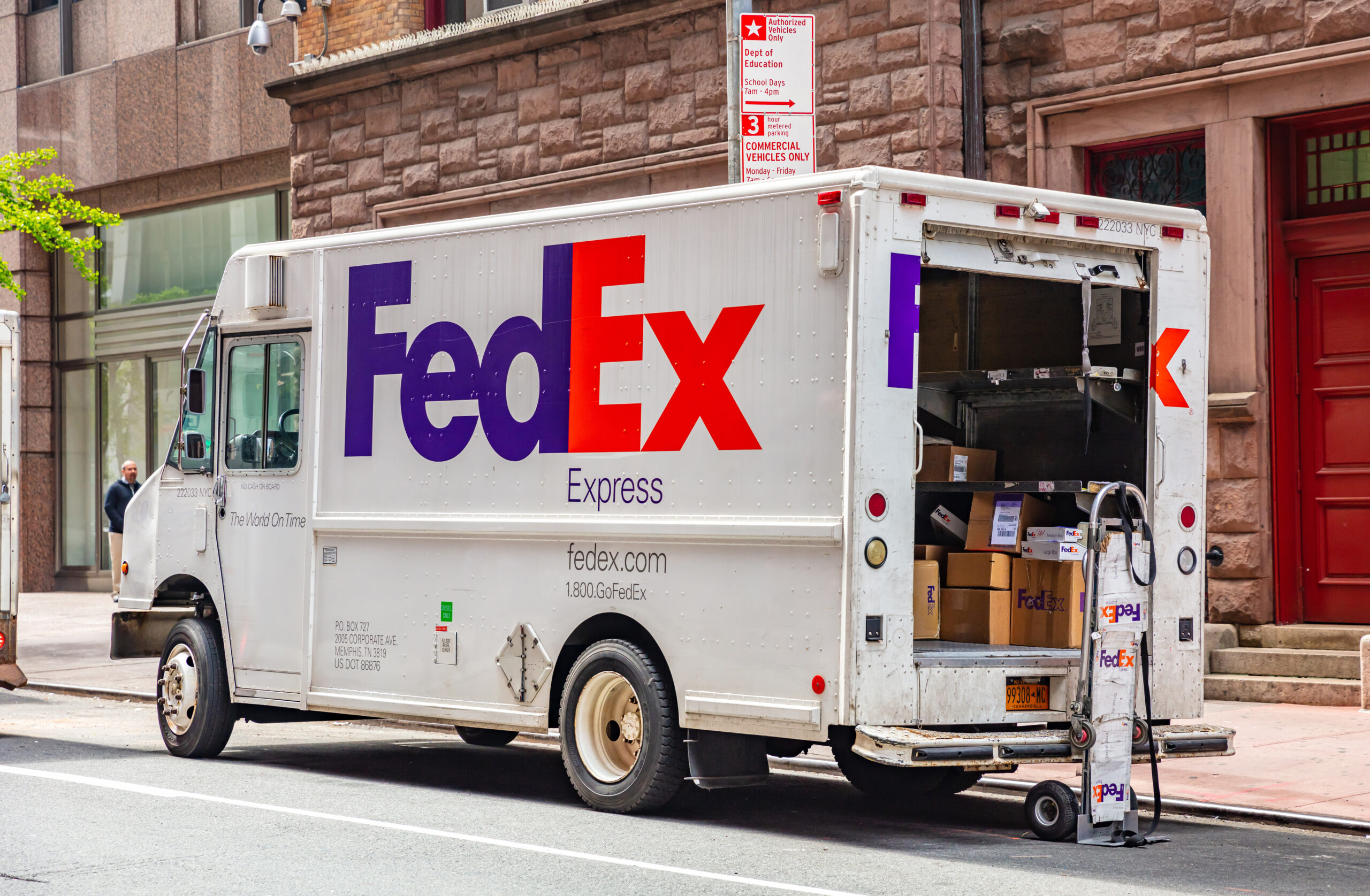 Packages in a FedEx truck with open door, parked on a street downtown
