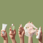Hands holding up Korean beauty and skin care products against a green background.