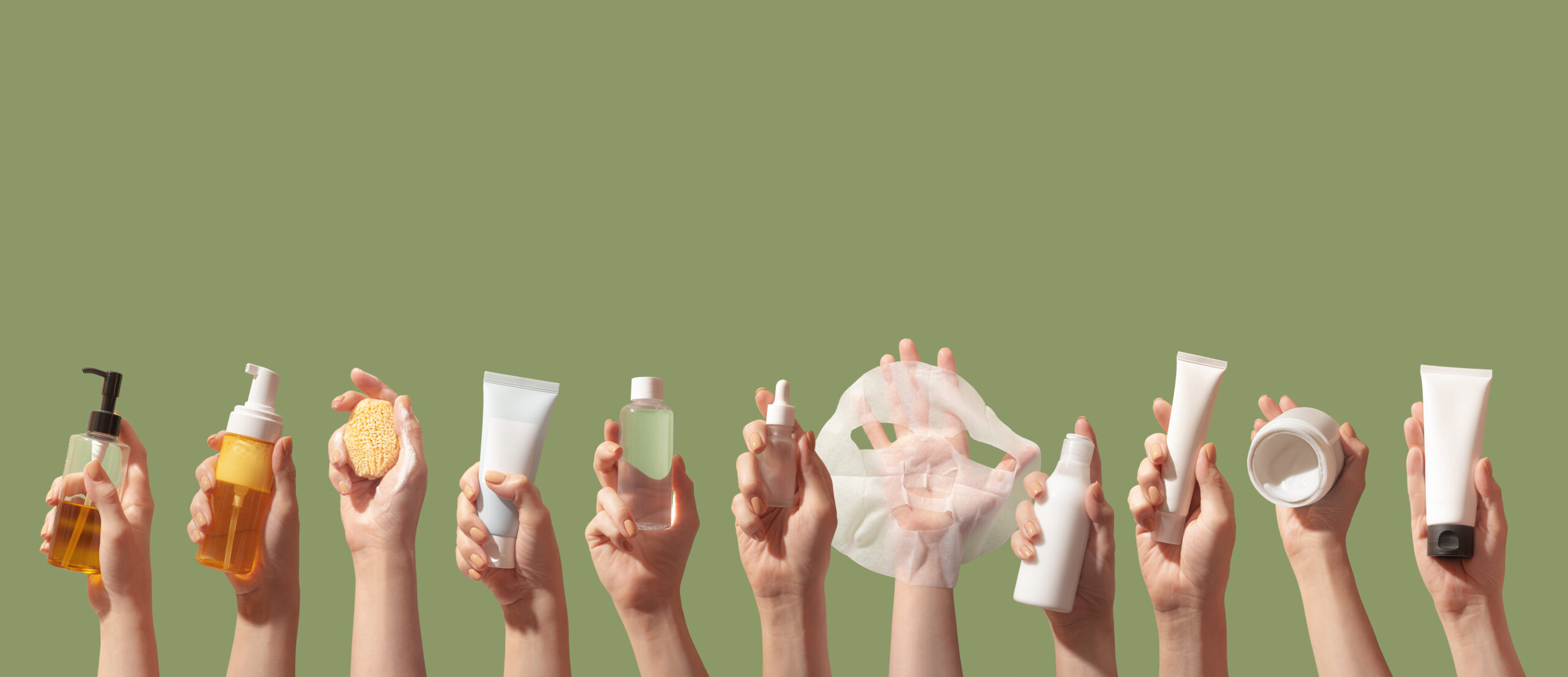 Hands holding up Korean beauty and skin care products against a green background.