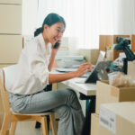 female entrepreneur on smartphone in room of cardboard boxes
