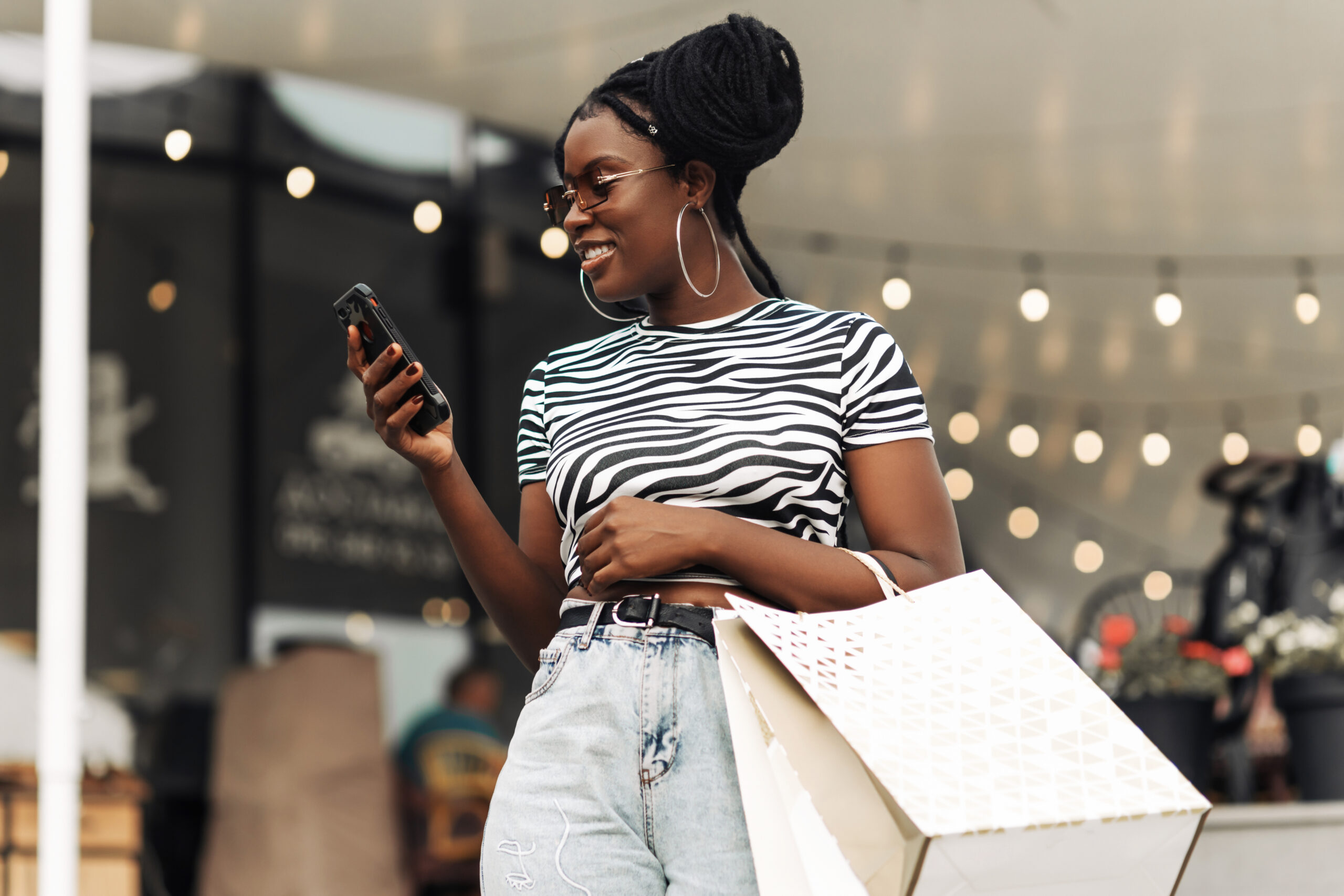 happy woman with shopping bags looks at mobile phone