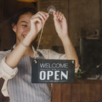 manager girl changing a sign from closed to open sign on door