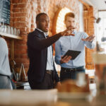 Coffee Shop Owners Meeting Behind the Counter and Working on Tablet Computer