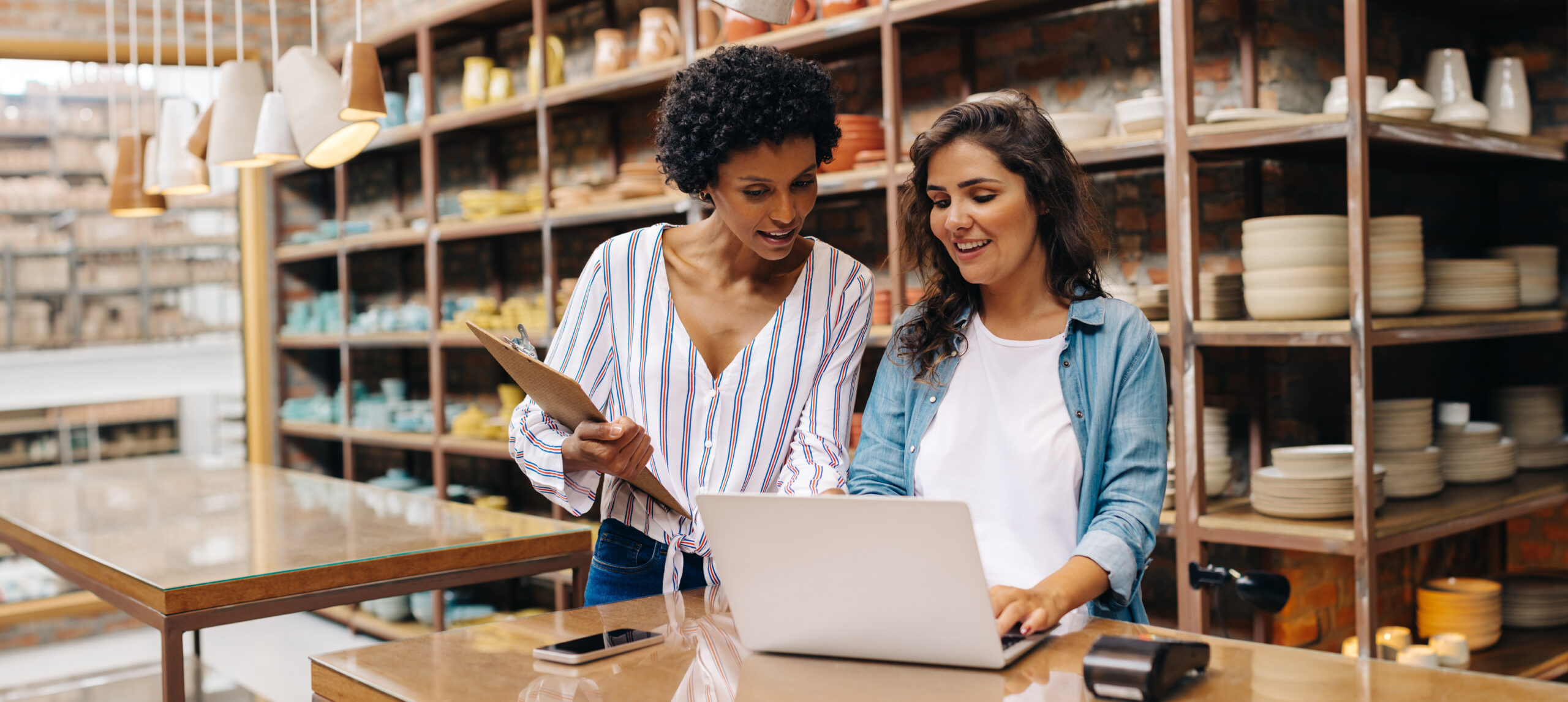 Two young shop owners using a laptop while working in a ceramic store.