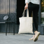 Woman holding white textile eco bag against urban city background.