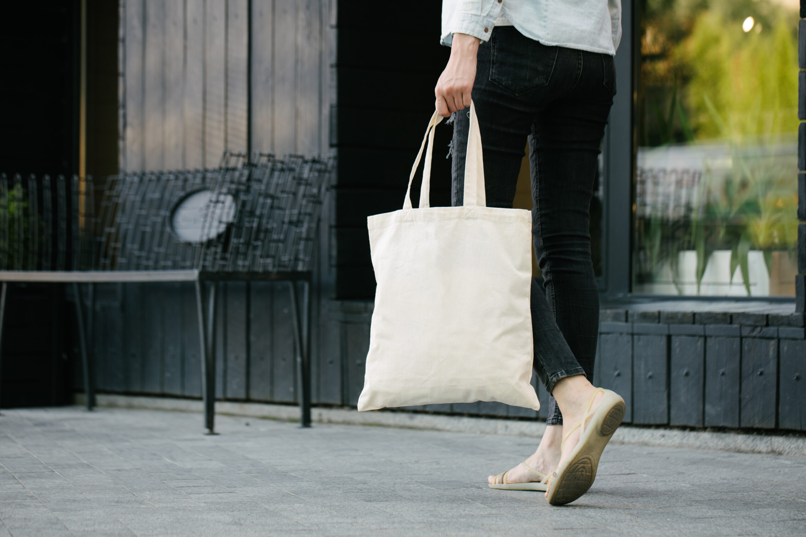 Woman holding white textile eco bag against urban city background.