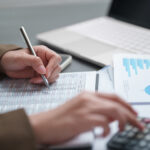 Businesswoman calculating and reviewing financial reports with charts and data at an office desk