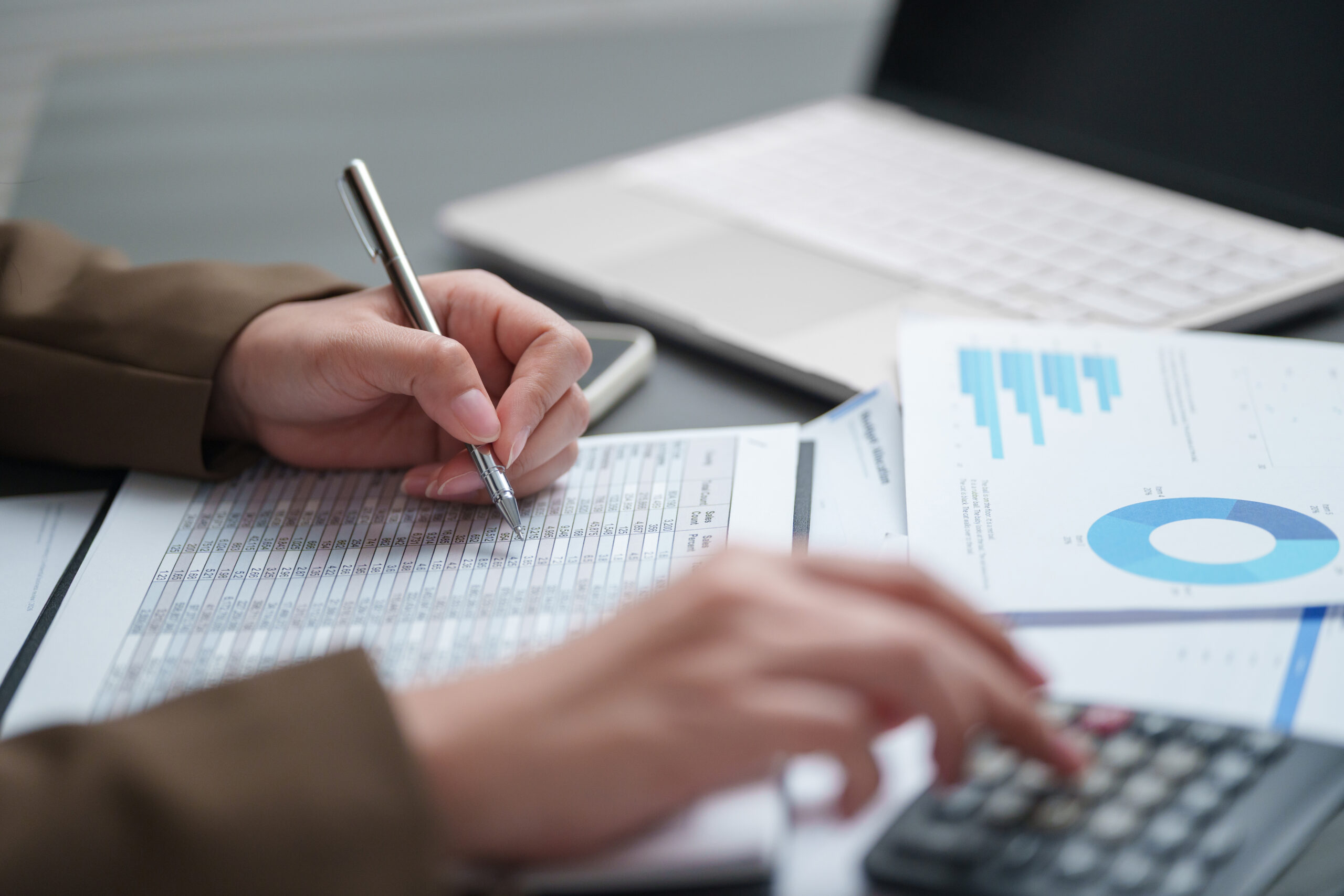 Businesswoman calculating and reviewing financial reports with charts and data at an office desk