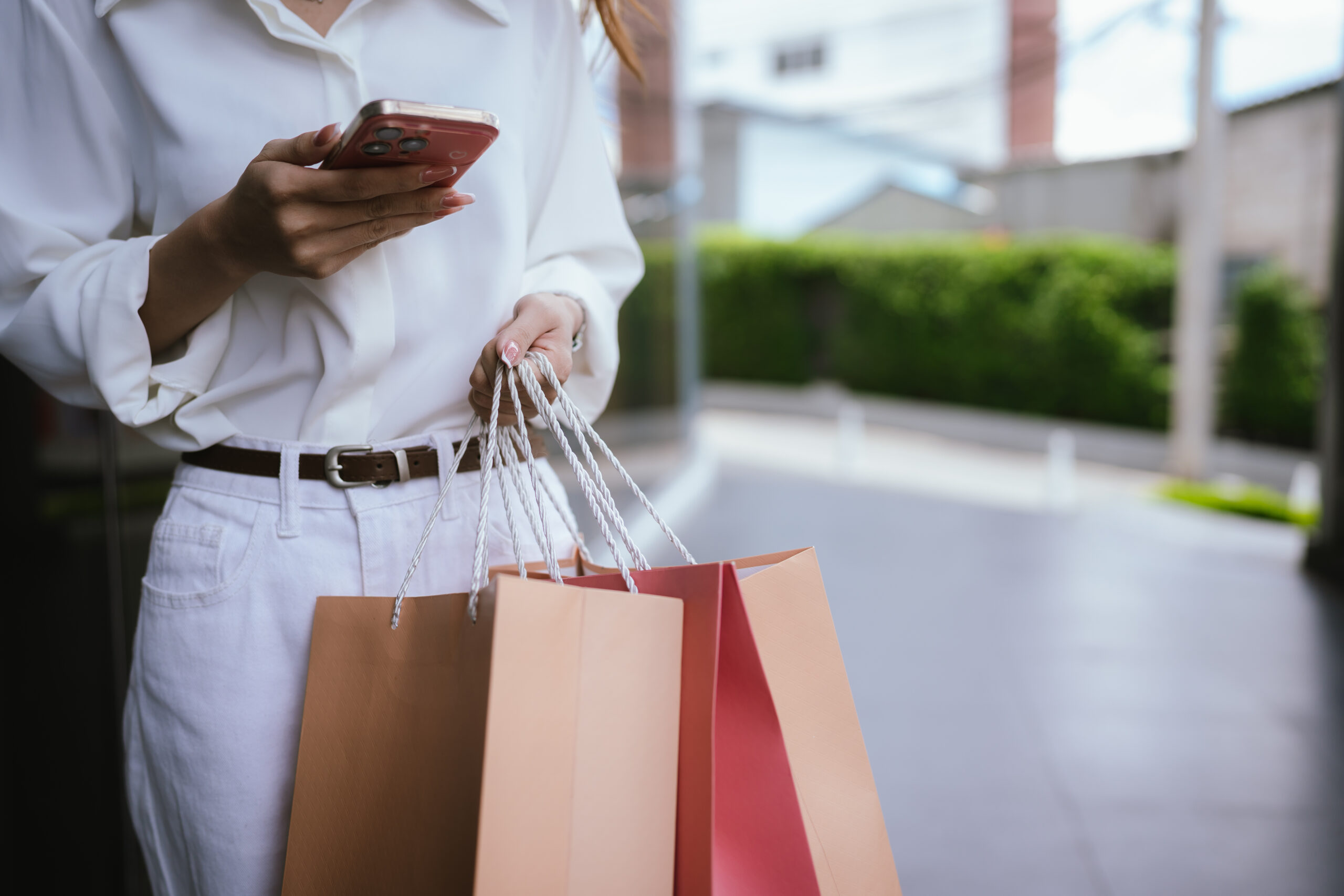 Close-up of a shopper carrying colorful shopping bags outdoors.