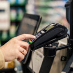 Male's hand entering credit card code at supermarket on pos terminal at self-service checkout.