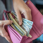 Woman taking out US dollar bills from her pocket wallet
