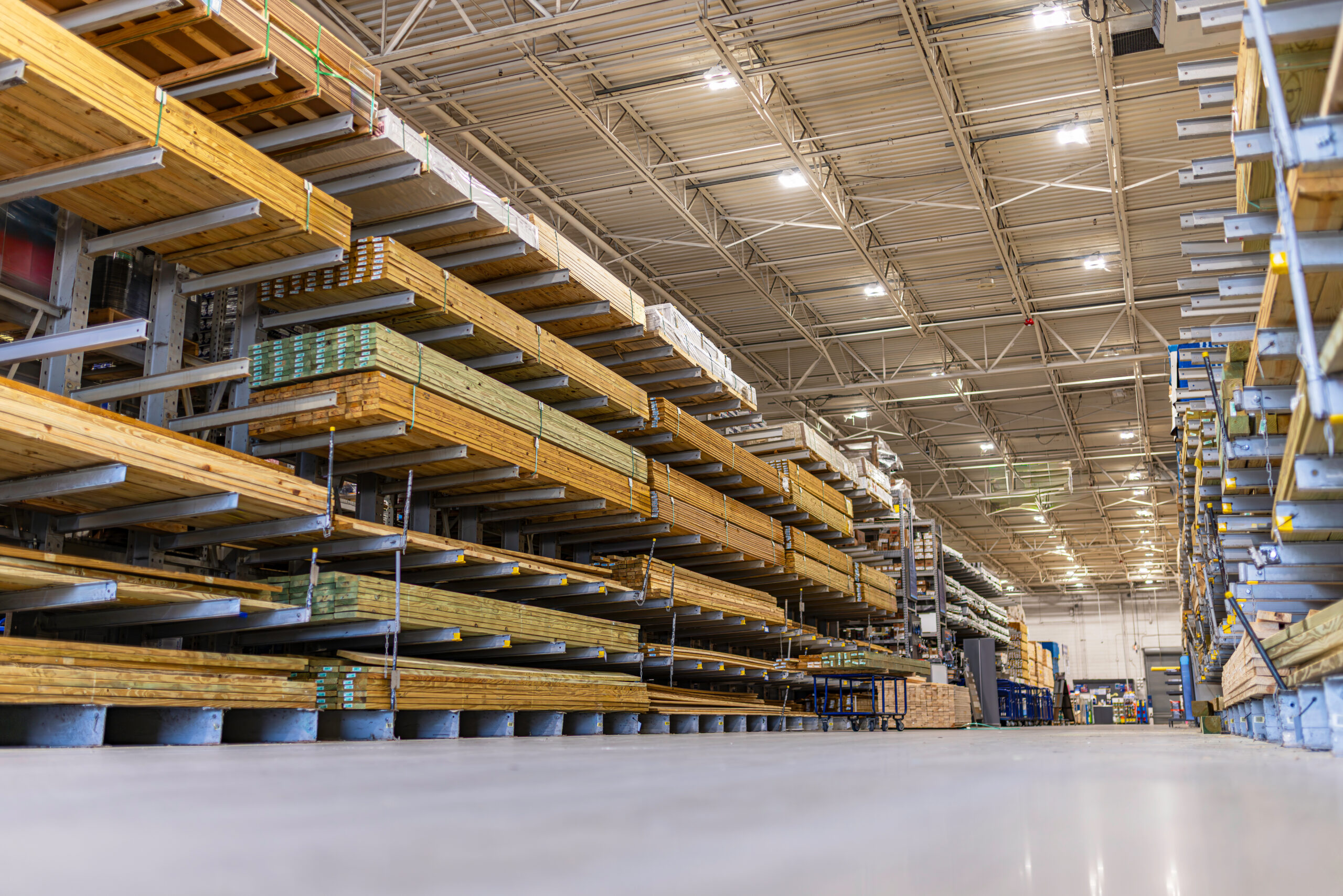 Low-angle view of organized stacks of lumber and pressure-treated wood boards stored on heavy-duty cantilever racks inside a large warehouse store